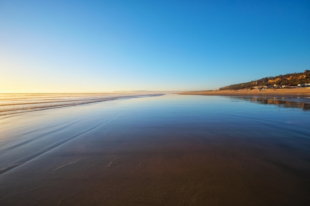 Atlantischer Ozeansonnenuntergang mit wogenden Wellen am Strand von Fonte da Telha, Costa da Caparica, Portugal