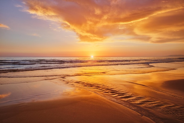 Atlantischer Ozeansonnenuntergang mit wogenden Wellen am Strand von Fonte da Telha, Costa da Caparica, Portugal