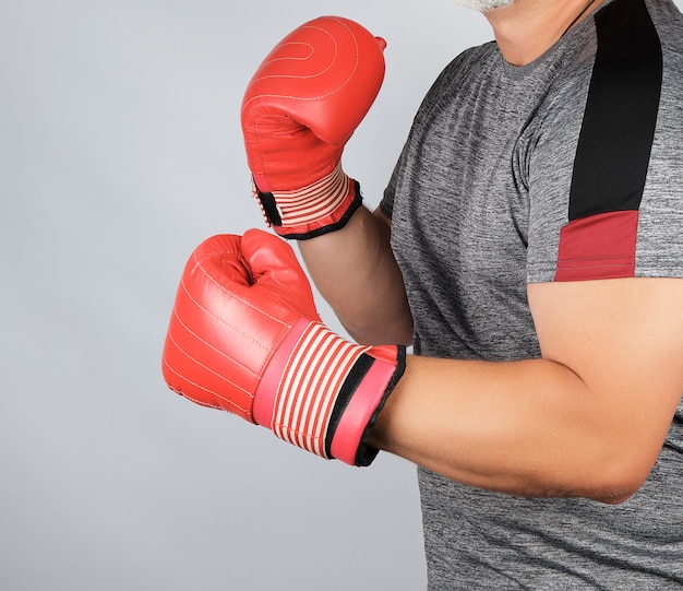 Atleta adulta muscular em uniforme cinza e luvas de boxe de couro vermelho