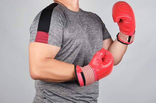 Atleta adulto musculoso en uniforme gris y guantes de boxeo de cuero rojo de pie en un estante