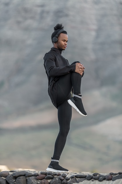 Atleta afro-americana, puxando a perna ao peito na natureza