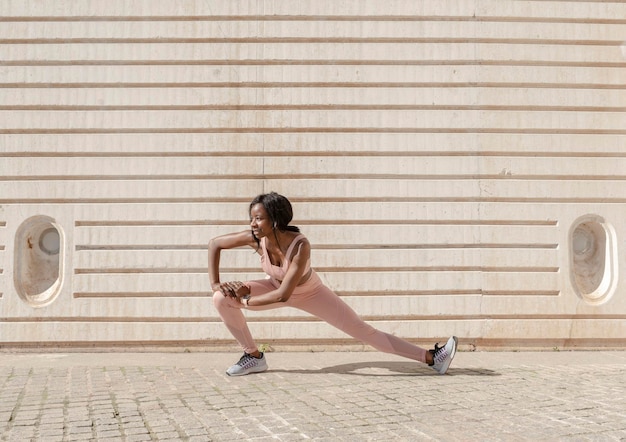 Una atleta afroamericana ejerciendo fitness al aire libre contra el calentamiento atlético de la pared y estirando el concepto de estilo de vida saludable
