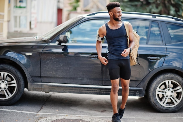 Atleta afroamericano hombre deportivo con mochila contra su auto todoterreno negro antes de entrenar