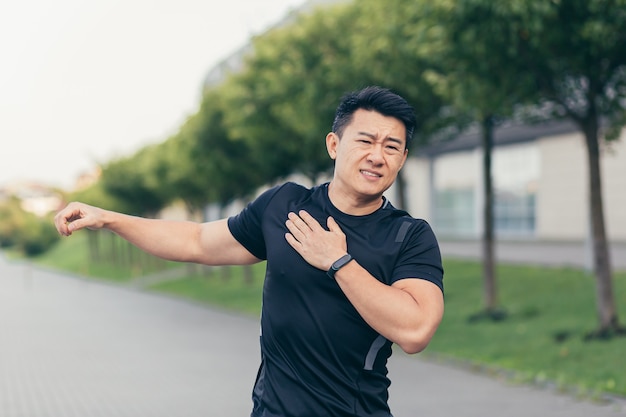 Atleta asiático, amassando dor no ombro, músculos do braço doloridos no parque