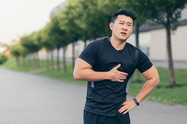 Atleta asiático do sexo masculino, tem dor no peito, fitness no parque e correndo, dor no coração após exercícios aeróbicos