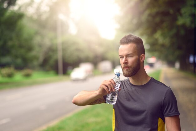 Atleta bonito a beber água na estrada.