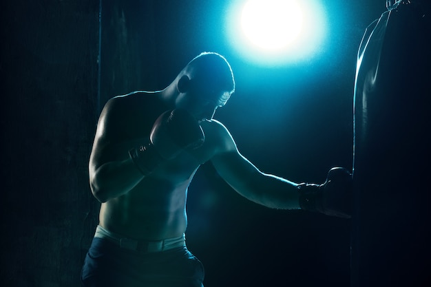 Atleta boxeador masculino socando um saco de pancadas com iluminação dramática em um estúdio escuro