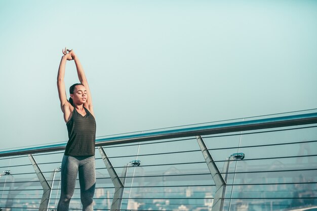 Atleta calmo em pé na ponte com os olhos fechados e esticando os braços para cima. Banner do site