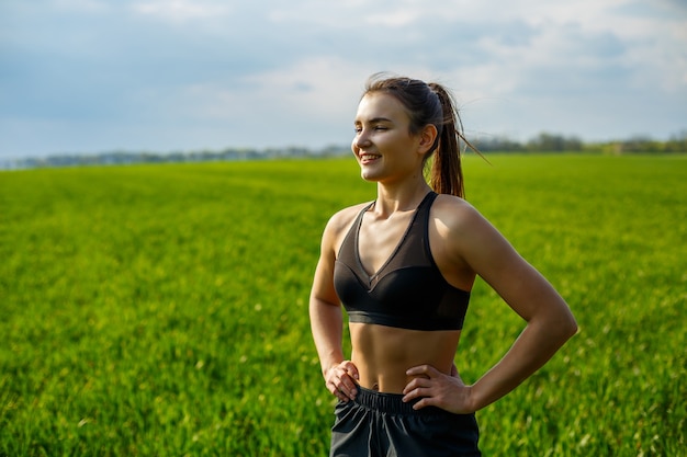 La atleta chica hace calentamiento al aire libre, ejercicios para los músculos. Mujer joven practica deportes, estilo de vida saludable, cuerpo atlético. Ella está en ropa deportiva, top negro y pantalones cortos. Concepto de deporte.