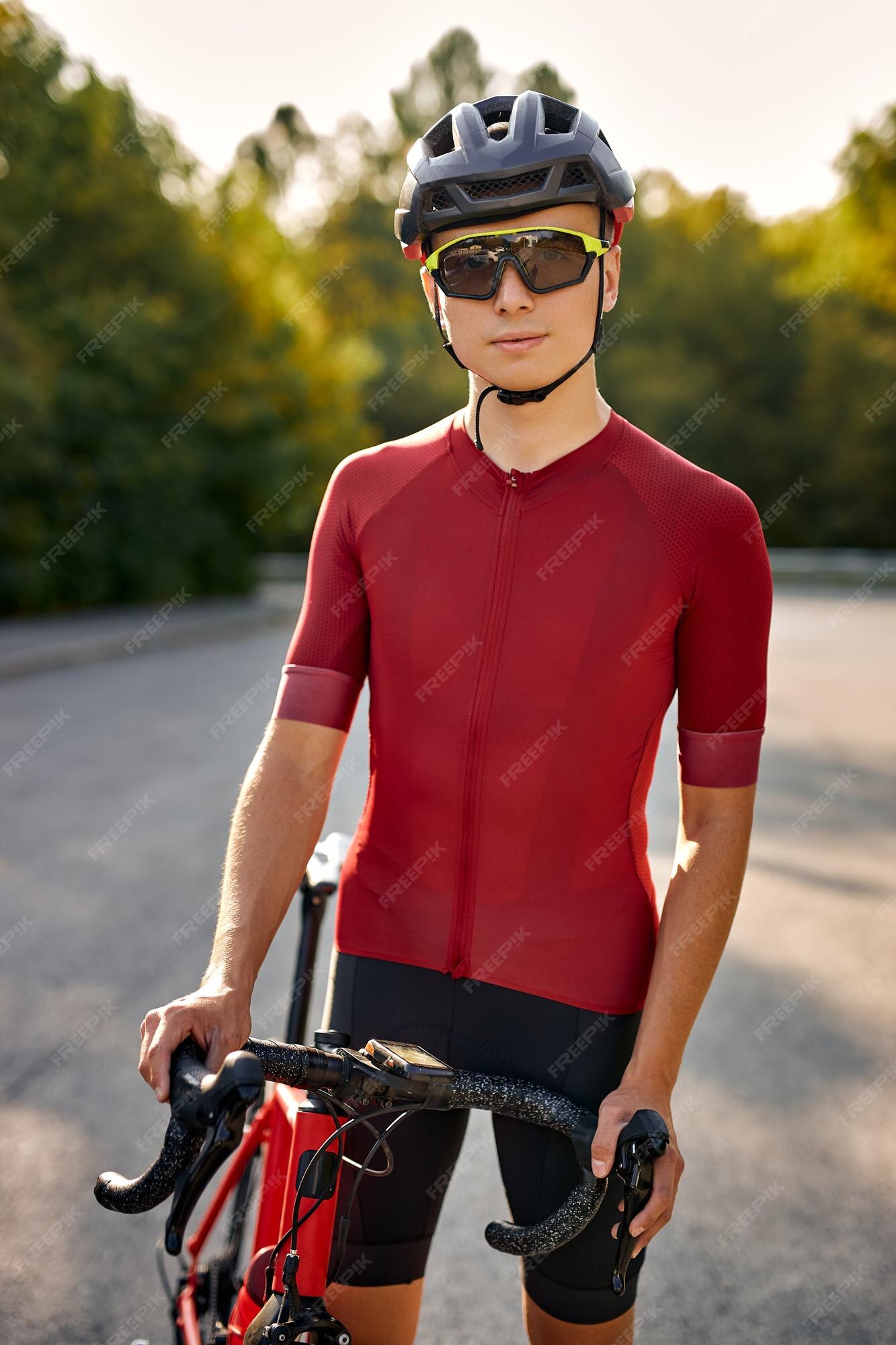 Atleta ciclista caucásico en ropa de ciclismo y casco mirando a la cámara descansando y relajándose después del en bicicleta en las calles del parque natural estilo de