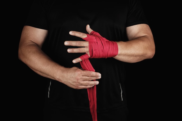 El atleta se coloca en la ropa negra y envuelve sus manos con una venda elástica textil roja antes de entrenar