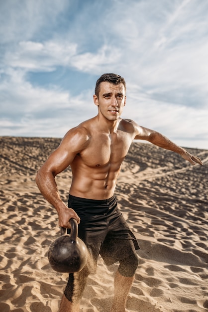 Atleta com kettlebell no deserto, voando na areia