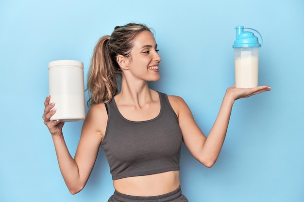 Atleta com shake de proteína e recipiente em estúdio azul