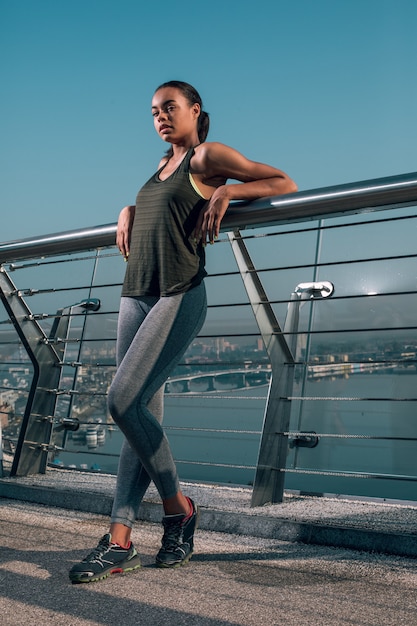 Atleta confiante em forma, em pé na ponte com os cotovelos no corrimão