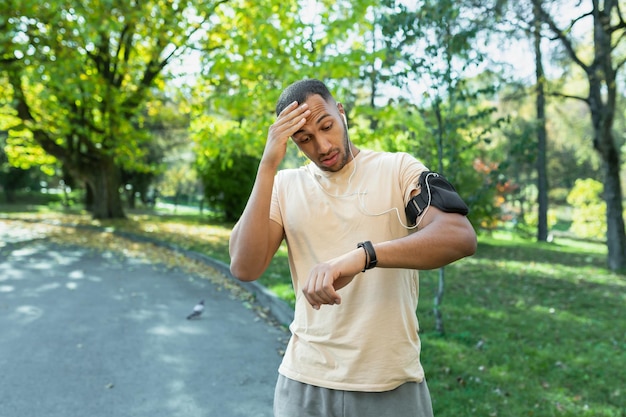 Atleta corredor jovem afro-americano no parque um homem cansado conta seu pulso em uma aptidão