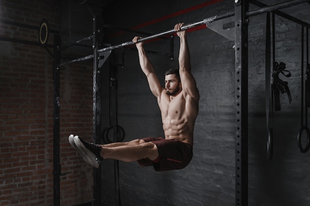 Foto atleta de crossfit haciendo ejercicio de abdominales en barra horizontal en el gimnasio