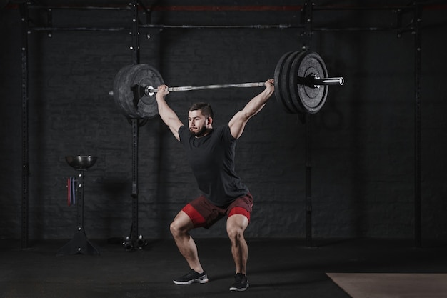 Atleta de crossfit joven levantando la barra sobre la cabeza en el gimnasio