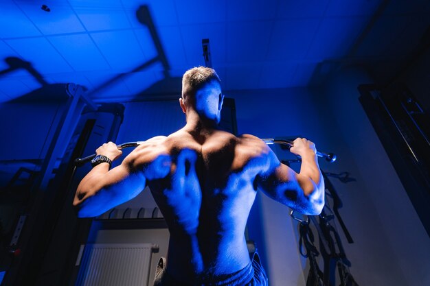 Atleta con cuerpo fuerte haciendo ejercicio empujando hacia arriba ejercicio en el gimnasio. Vista desde abajo. Filtro de luz azul.