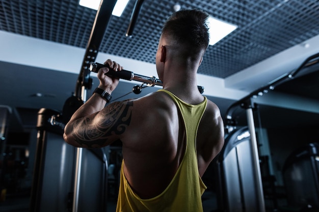 Atleta de homem com corpo musculoso em regata esportiva amarela fazendo exercício no ginásio moderno