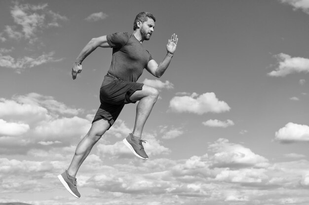 Foto atleta de homem energético com corpo musculoso executado em roupas esportivas ao ar livre na motivação de fundo do céu