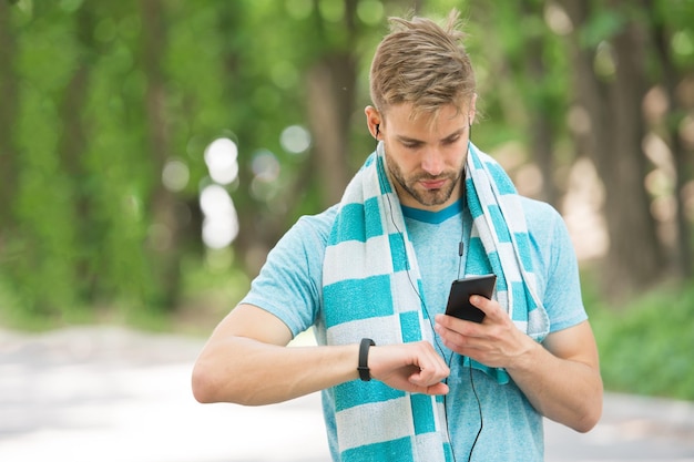 Atleta de homem no rosto ocupado configurando o fundo da natureza do rastreador de fitness Treinamento de esportista com gadget de pedômetro Atleta com cerdas com rastreador de fitness ou conceito de gadget de esporte pedômetro