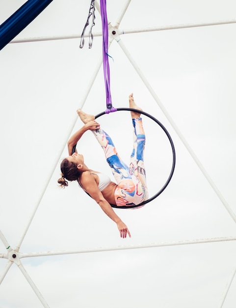 Atleta de menina jovem fitness corpo perfeito fazendo exercícios aéreos com um círculo