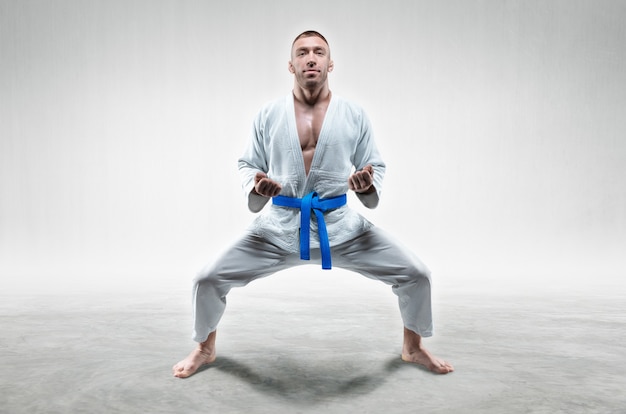 Atleta de quimono com faixa azul fica em posição de combate. conceito de caratê, sambo, jiu-jitsu. mídia mista