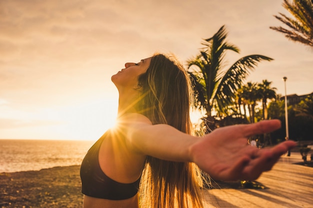 Atleta deportivo y hermosa joven estirar y respirar después del entrenamiento al aire libre con puesta de sol y luz solar en escena con océano y cielo