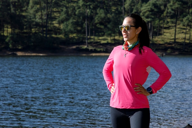 Atleta descansando en la orilla de un lago despues de correr en el bosque rodeado de arboles