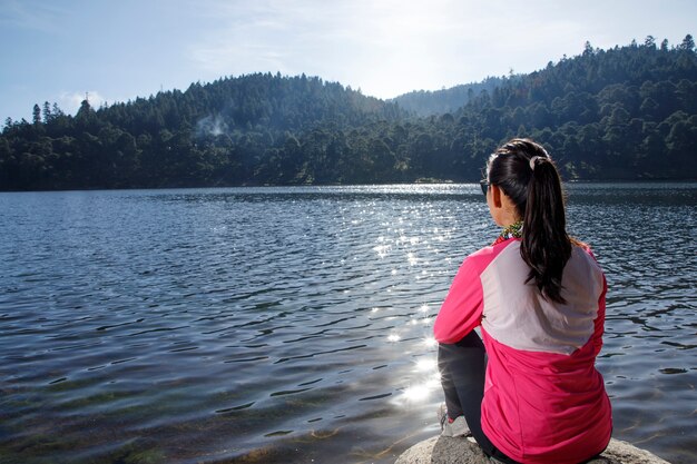 Atleta descansando a la orilla de un lago sentada sobre una piedra después de correr en el bosque