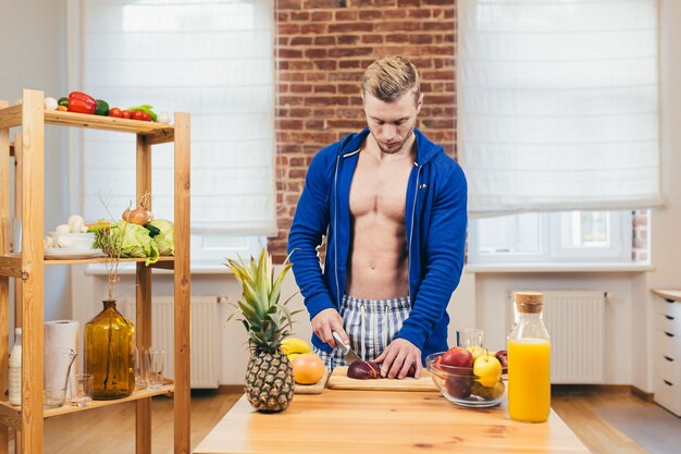Atleta do sexo masculino prepara salada e suco de frutas frescas em casa na cozinha