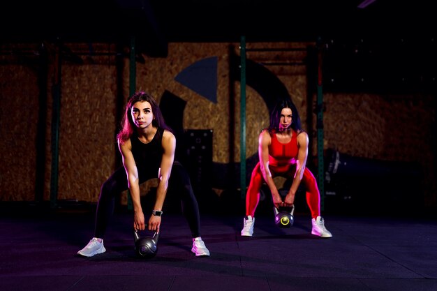 Atleta de dos mujeres del ajuste atractivo que realiza un swing de kettle-bell en el gimnasio.