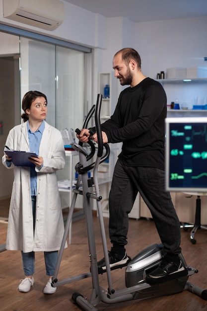 Atleta em equipamentos esportivos trabalhando na resistência do corpo durante o exame médico no laboratório clínico, enquanto uma pesquisadora especialista analisando dados de ekg medindo o pulso de freqüência cardíaca. serviço de remédios