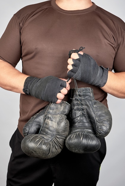 Atleta em roupas marrons detém luvas de boxe pretas de couro vintage muito antigo