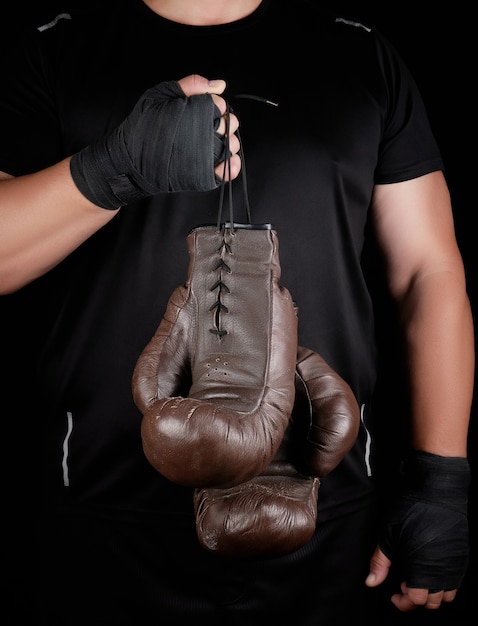 Atleta em roupas pretas segura luvas de boxe marrons de couro vintage muito antigas