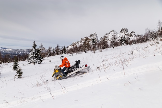 Atleta em um snowmobile movendo-se na floresta de inverno