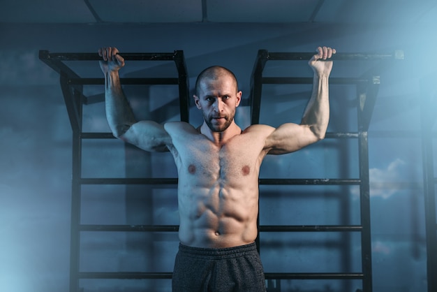 Atleta con entrenamiento de cuerpo musculoso en barra horizontal en gimnasio.