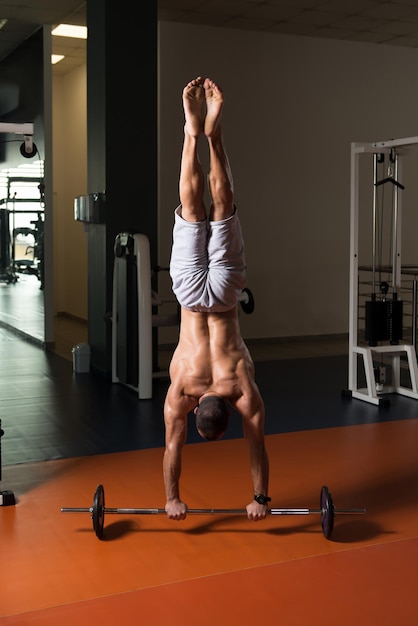 Atleta exercitando flexões de parada de mão na barra na academia