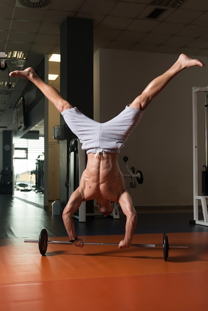 Atleta exercitando flexões de parada de mão na barra na academia