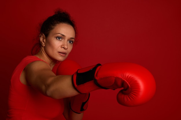 Atleta femenina boxeadora decidida peleas en guantes de boxeo rojos sobre un fondo rojo. Concepto de arte marcial con espacio de copia para publicidad para el evento del día del boxeo