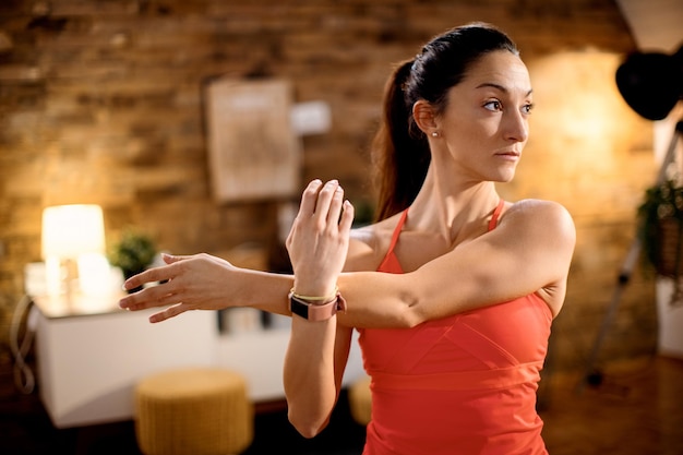 Atleta femenina estirando su brazo mientras hace ejercicio en casa