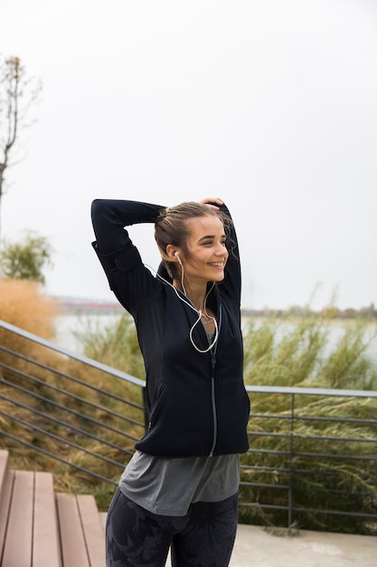 Foto atleta femenina estirando sus brazos mientras escucha música al aire libre