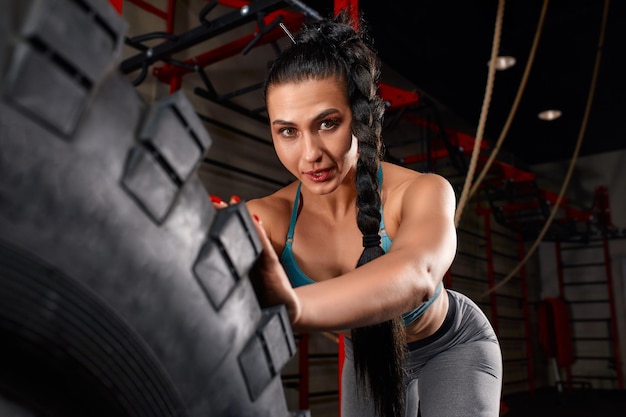 Una atleta femenina en forma haciendo ejercicio con un neumático enorme girando y volteando en el gimnasio Mujer Crossfit haciendo ejercicio con un neumático grande