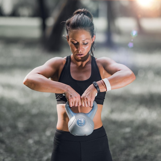 Atleta femenina haciendo ejercicio con pesas rusas en el parque