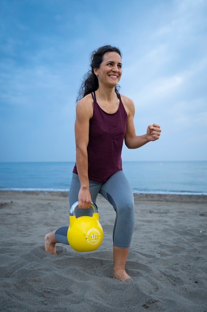 Atleta femenina haciendo ejercicio en la playa con kettle bells