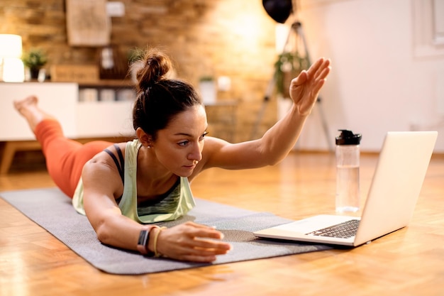 Atleta femenina haciendo ejercicio en el suelo mientras sigue una clase de entrenamiento en línea con una laptop