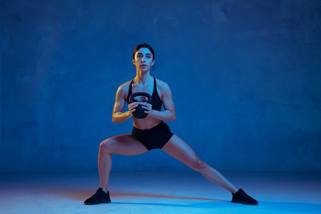 Atleta femenina joven caucásica practicando sobre fondo azul de estudio en luz de neón