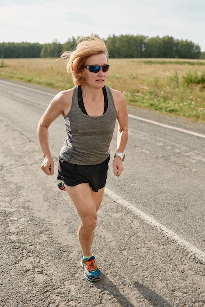 Atleta femenina en ropa deportiva corriendo en una carretera por la mañana