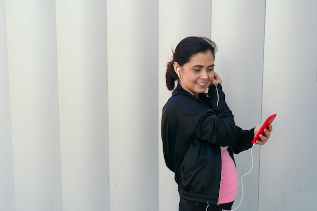 Atleta femenina con smartphone poniéndose auriculares y empezando a escuchar música mientras entrena.