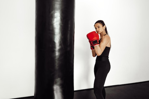 Atleta feminina com luvas de boxe vermelhas bate em uma pêra em uma academia